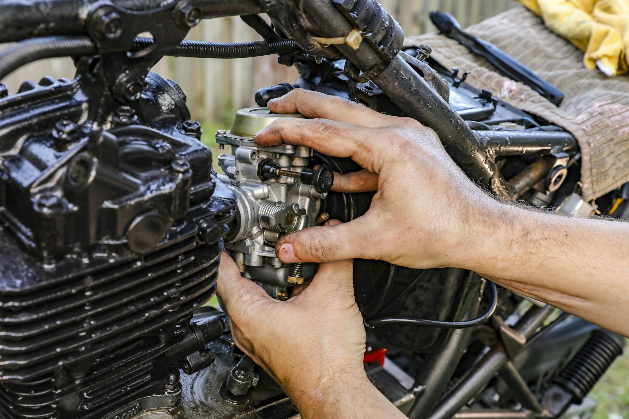 Close-up of a mechanic's hands assembling a motorcycle carburetor outdoors.